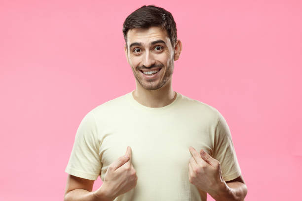 övergripande bild av unga positiva europeiska mannen i casual beige t-shirt isolerad på rosa bakgrund ser glad och blyg, pekar på sig själv med fingrarna på båda händerna, tittar förvånad och lugna - endast en man bildbanksfoton och bilder