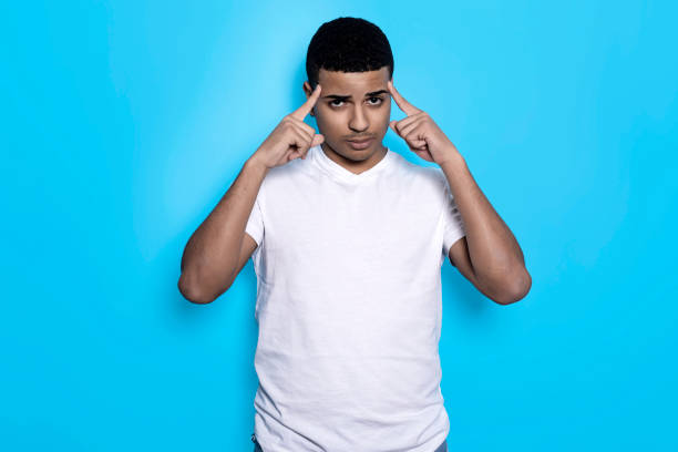 Horizontal portrait of black man in white t-shirt with fingers on temples, isolated on blue background stock photo
