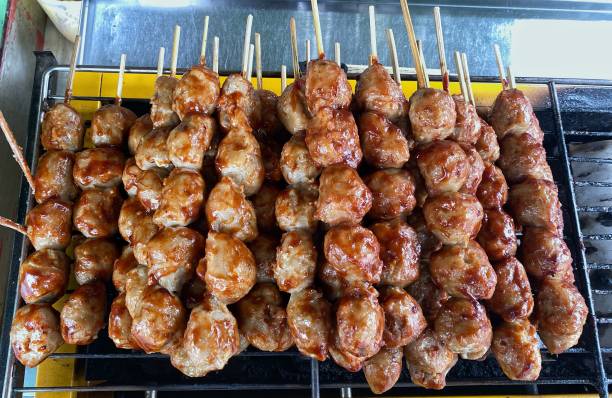 A horizontal shot of a pile of meatballs skewered using bamboo after being grilled using soy sauce and tomatoes stock photo