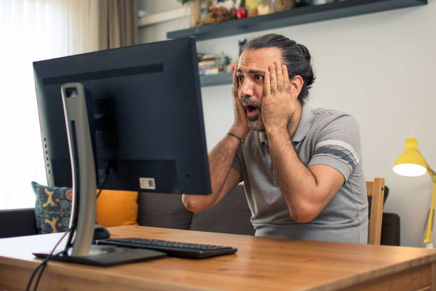 Horrified man working at home on desktop pc stock photo