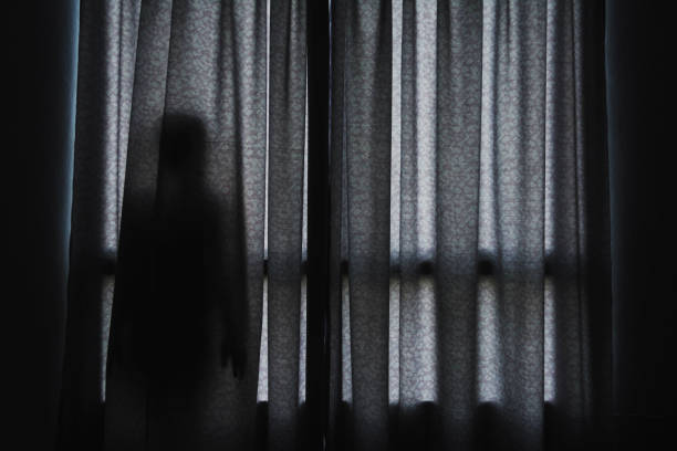 horror scene of woman's shadow standing hiding behind curtain stock photo