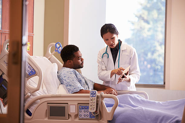 Hospital Doctor With Digital Tablet Talks To Male Patient Hospital Doctor With Digital Tablet Talks To Male Patient patient in hospital bed stock pictures, royalty-free photos & images