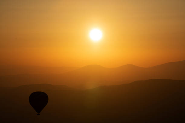 hot air balloon silhouette with sun rising over the mountains stock photo