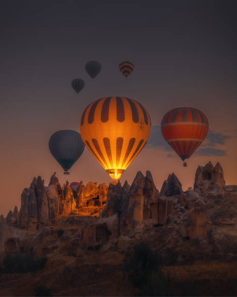 Hot Air balloons flying over rock formations at sunrise in Cappadocia, Goreme, Turkey Spectacular sunset landscape view of hot air balloon illuminated with fire in sky tour over amazing fairy chimneys rock forms on valleys and fields in early morning in Kapadokya, Göreme National Park, Turkiye. Dreamy nature background. türkiye country stock pictures, royalty-free photos & images