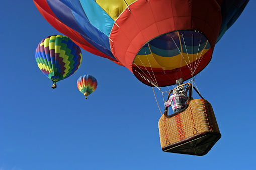 A brightly colored hot air balloon ascends into a cloudless blue sky, where two other balloons await.
