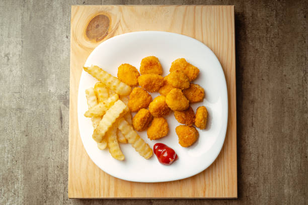 Hot chicken nuggets and french fries with a little tomato sauce on a plate on a wooden surface stock photo