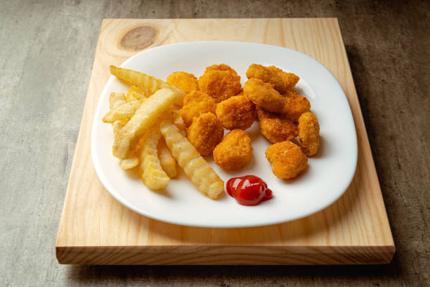 Hot chicken nuggets and french fries with a little tomato sauce on a plate on a wooden surface stock photo
