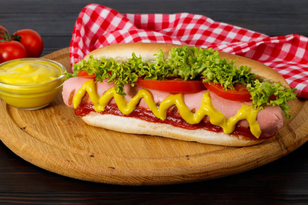 Hot dog with mustard, tomato and lettuce on wooden background stock photo