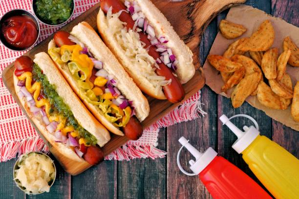 Hot dogs with assorted toppings and potato wedges, overhead scene on wood Hot dogs with assorted toppings and potato wedges, overhead scene on a rustic wood background condiment stock pictures, royalty-free photos & images