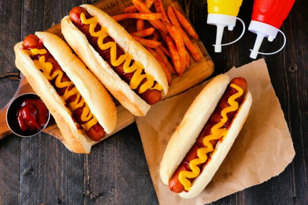 Hot dogs with mustard, ketchup and fries overhead scene Traditional hot dogs with mustard, ketchup and fries. Top view scene on a rustic wood background. hot dog stock pictures, royalty-free photos & images