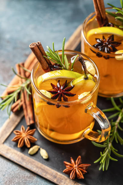 Hot drink cocktail for New Year, Christmas, winter or autumn holidays. Toddy. Mulled pear cider or spiced tea or grog with lemon, pear, cinnamon, anise, cardamom, rosemary. stock photo