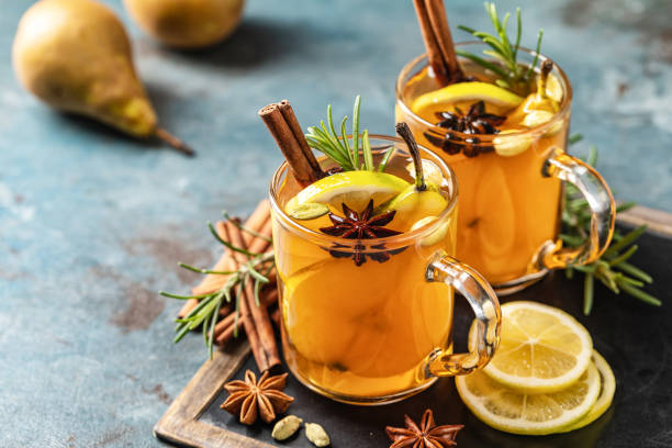 Hot drink cocktail for New Year, Christmas, winter or autumn holidays. Toddy. Mulled pear cider or spiced tea or grog with lemon, pear, cinnamon, anise, cardamom, rosemary. stock photo