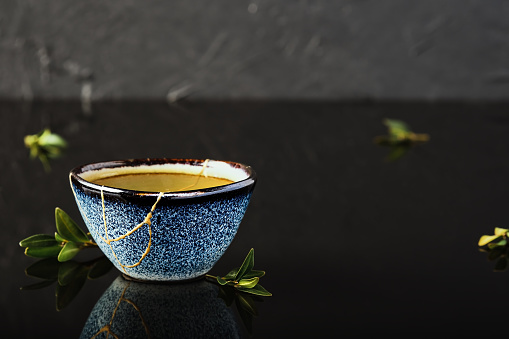 Hot green tea bowl, Japanese tea on a dark background. Selective focus on the cup. Reclaimed ceramic blue cup, second life of things, recycling