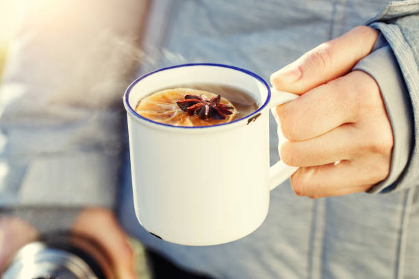 Hot mulled cider or spiced tea mug in woman hand outdoor stock photo