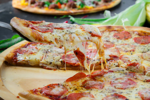 Hot pizza slice with melting cheese on a rustic dark wooden table. stock photo