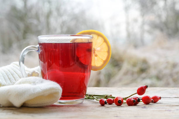 Hot red rose hip tea with a lemon slice in a glass mug on a rustic wooden table against a frosty winter landscape, copy space stock photo
