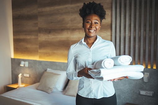 Hotel maid bringing fresh towels to the room. Maid clean the room and replace the bedsheets and towels. Maid with fresh towels in hotel room