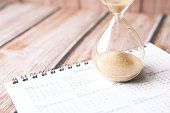 istock hourglass on calendar on table, sand flowing through the bulb of sandglass 1325166624