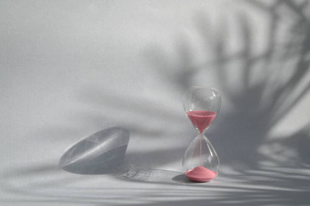 Hourglass sand timer with palm shadow on wall. stock photo