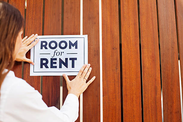 house owner attaching "Room for rent" sign on a wall