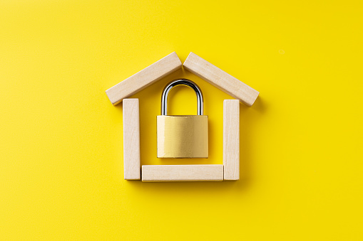 house symbol made by wooden blocks over yellow background with padlock inside. outer space. home protection and security concept.