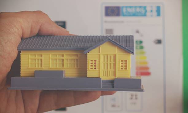  main tenant une petite maison en plastique devant une étiquette énergétique