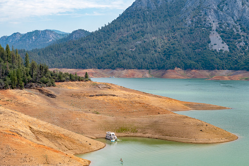 Houseboats and other recreational vehicles on Shasta Lake, California during drought. Water level is about 130 feet/40 meters below full capacity of 518 feet/160 meters exposing baren shoreline. July 30, 2022.