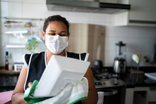 Housekeeper washing the dishes wearing protective mask Housekeeper washing the dishes wearing protective mask maid stock pictures, royalty-free photos & images