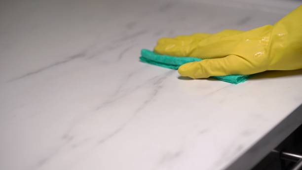 A housewife in yellow rubber gloves washes and wipes a marble kitchen countertop A housewife in yellow rubber gloves washes and wipes a marble kitchen countertop, table or surface with a wet green rag with detergent. Woman cleaning house, cleaning service. Housekeeper disinfecting Marble cleaning stock pictures, royalty-free photos & images