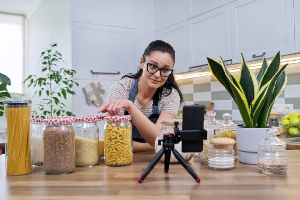 Housewife recording video reviewing products on smartphone at home in the kitchen Housewife woman blog, female recording video reviewing products on smartphone at home in the kitchen. Blogging, vlog, technology, lifestyle, hobbies and leisure, people concept plant-based marketing stock pictures, royalty-free photos & images