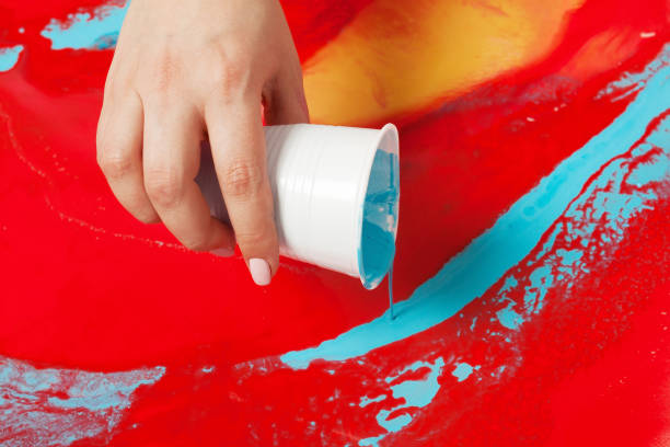 How to make acrylic painting. Work in progress. Female hand holding a plastic cup with blue paint. stock photo