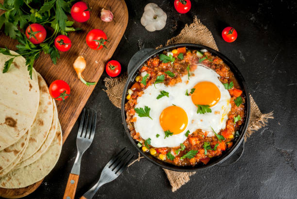 Huevos rancheros, Mexican food Traditional Mexican dish Huevos rancheros - scrambled eggs with tomato salsa, with taco tortillas, fresh vegetables and parsley. Breakfast for two. Top view. With a forks, copy space poached food photos stock pictures, royalty-free photos & images