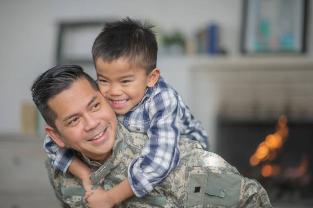 Hugging Dad A military dad and his son are hugging in their living room. The son is smiling happily at the camera. filipino family stock pictures, royalty-free photos & images