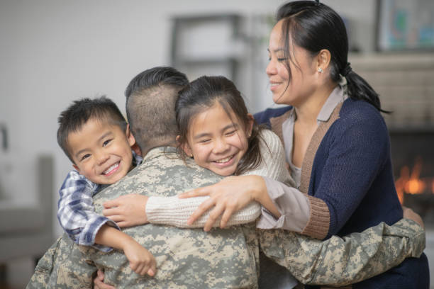 A family of four are hugging in the living room. They are happy to see the dad, who is wearing military gear.