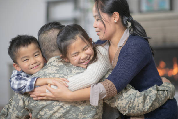 Hugging Family A family of four are hugging in the living room. They are happy to see the dad, who is wearing military gear. veterans returning home stock pictures, royalty-free photos & images