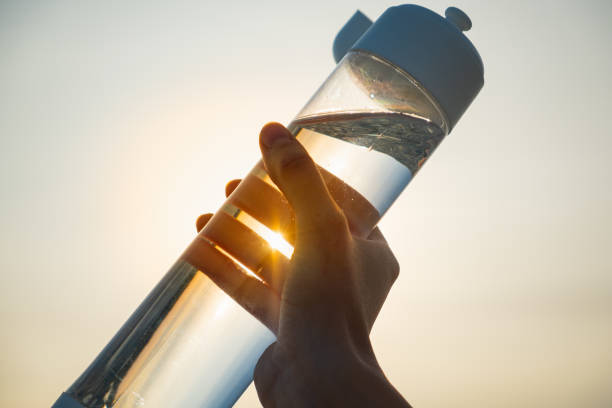 Human hand holds a water bottle against the setting sun. stock photo
