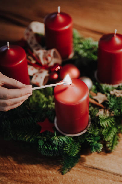 menschliche hand, die am ersten adventssonntag vier wochen bis weihnachten die erste kerze des adventskranzes anzündet. - adventskranz stock-fotos und bilder