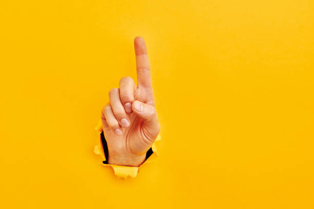 Human hand reaching through torn yellow paper sheet showing number one stock photo