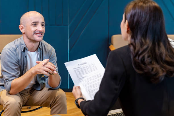 Human resource manager is interviewing new applicant while looking at the resume for work experience profile stock photo