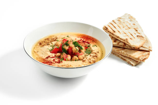 Hummus with spices, chickpeas, tomatoes and pita bread in a bowl isolated on a white background stock photo