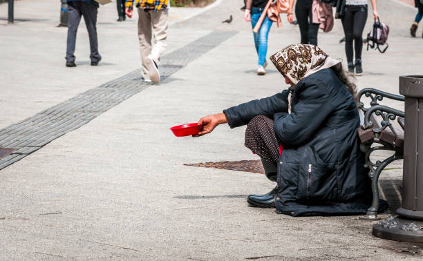 Hungry homeless beggar woman beg for money on the urban street in the city from people walking by, social documentary concept stock photo
