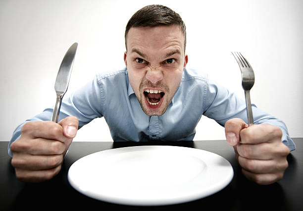 Hungry! man sitting on a table in front of an empty plate. knife and fork in his hands.he is screaming. he is hungry. hungry stock pictures, royalty-free photos & images