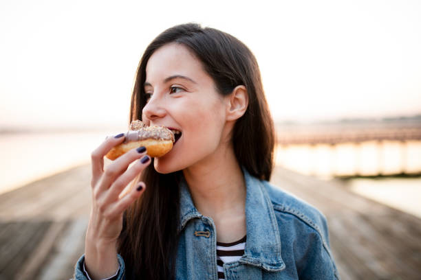 Hungry woman eating donut Young beautiful woman eating chocolate donut in nature sugar food stock pictures, royalty-free photos & images
