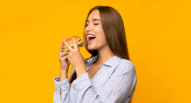 jeune femme affamé mangeant le hamburger restant dans le studio, panorama - eating burger photos et images de collection