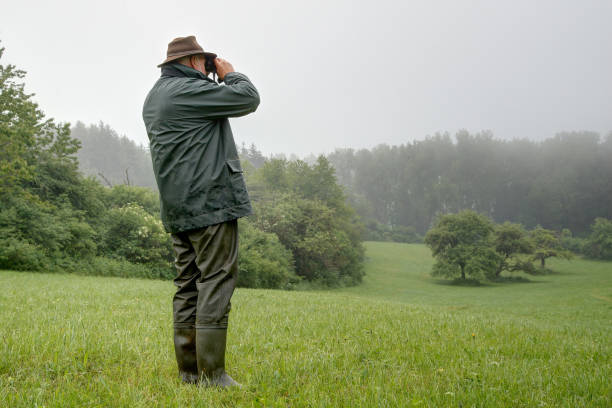 Hunter in the rain, watch a small idyllic valley through his binoculars. stock photo