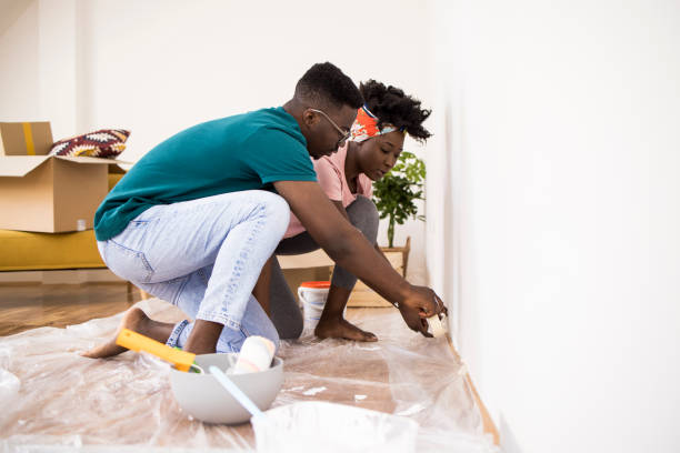 Husband helping wife while painting apartment together stock photo