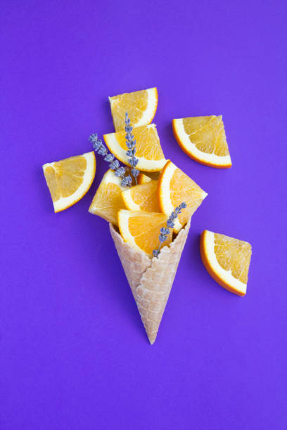 Ice cream cone with chopped orange fruit and lavender flower on the purple background. Top view. Copy space. stock photo