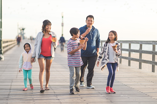 An attractive Filipino couple and their three children eat ice cream cones as they walk down a California boardwalk by the beach