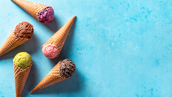 Various ice cream scoops in cones with copy space. Colorful ice cream in cones chocolate, strawberry, blueberry, pistachio or matcha, biscuits chocolate sandwich cookies on blue background. Top view