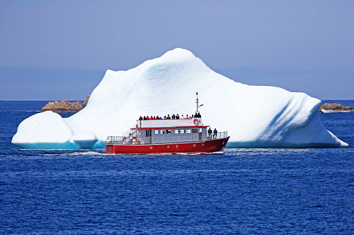 A tour boat sailing close to an iceberg in Newfoundland, Canada.  Twillingate Gate, NL
